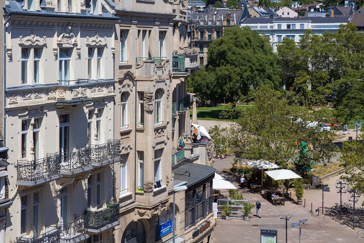 Un bâtiment historique à l’architecture riche et ornée, une rue bordée de voitures garées et un ciel bleu dégagé.
