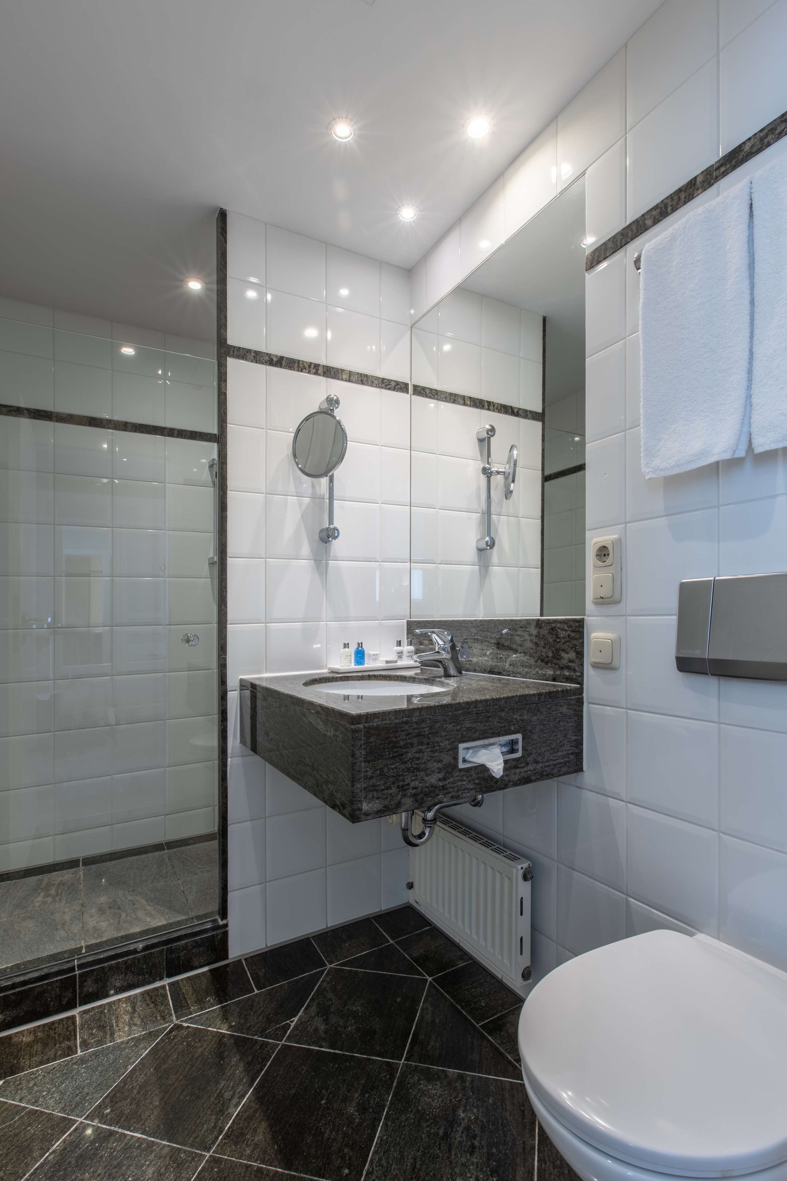 Een moderne badkamer met een douchecabine van glas, een marmeren wastafel en een wit toilet.