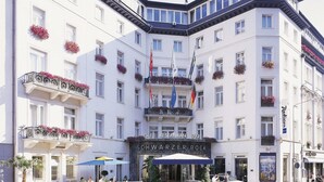 Un hotel de estilo arquitectónico europeo clásico, con varios balcones adornados con jardineras, banderas y una entrada destacada que muestra el cartel “SCHWARZER BOCK”.