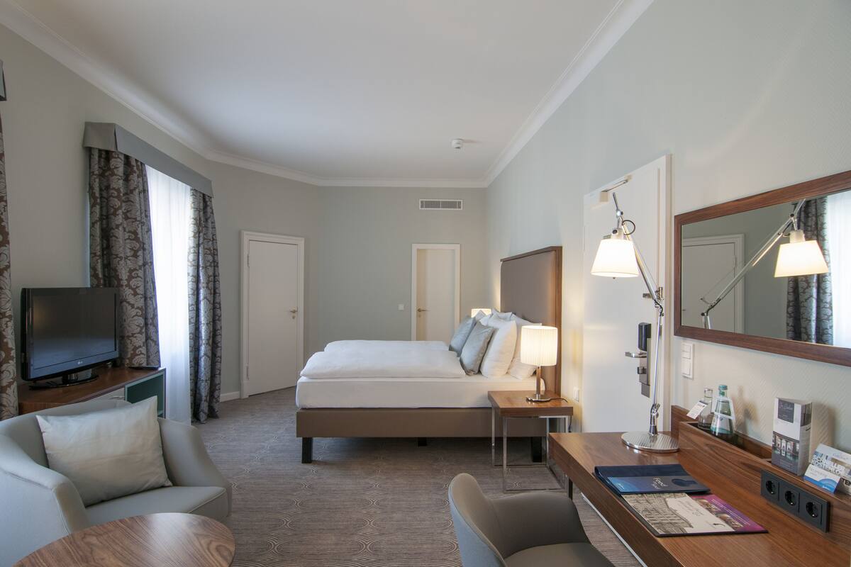Une chambre d’hôtel avec un lit, un bureau avec une lampe, une télévision et une chaise.