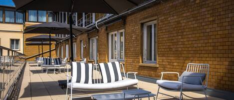 Una terraza con mobiliario exterior, incluyendo sillones y mesas, y sombrillas que dan sombra.