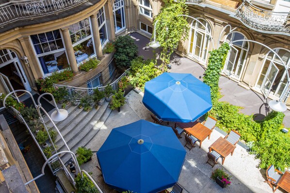 Vista aérea de un patio con dos sombrillas azules, mesas al aire libre y abundante vegetación.