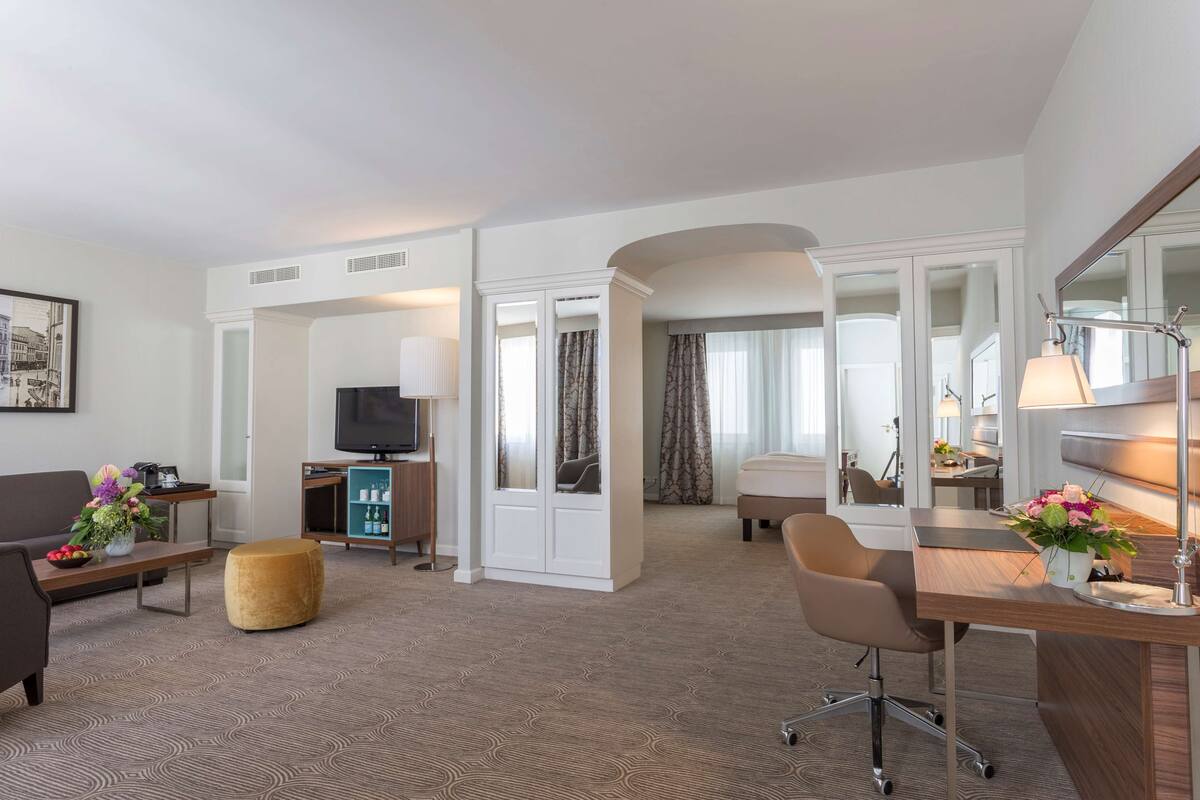 Une chambre d’hôtel comprenant un coin salon, un bureau avec une lampe, une télévision et un canapé.