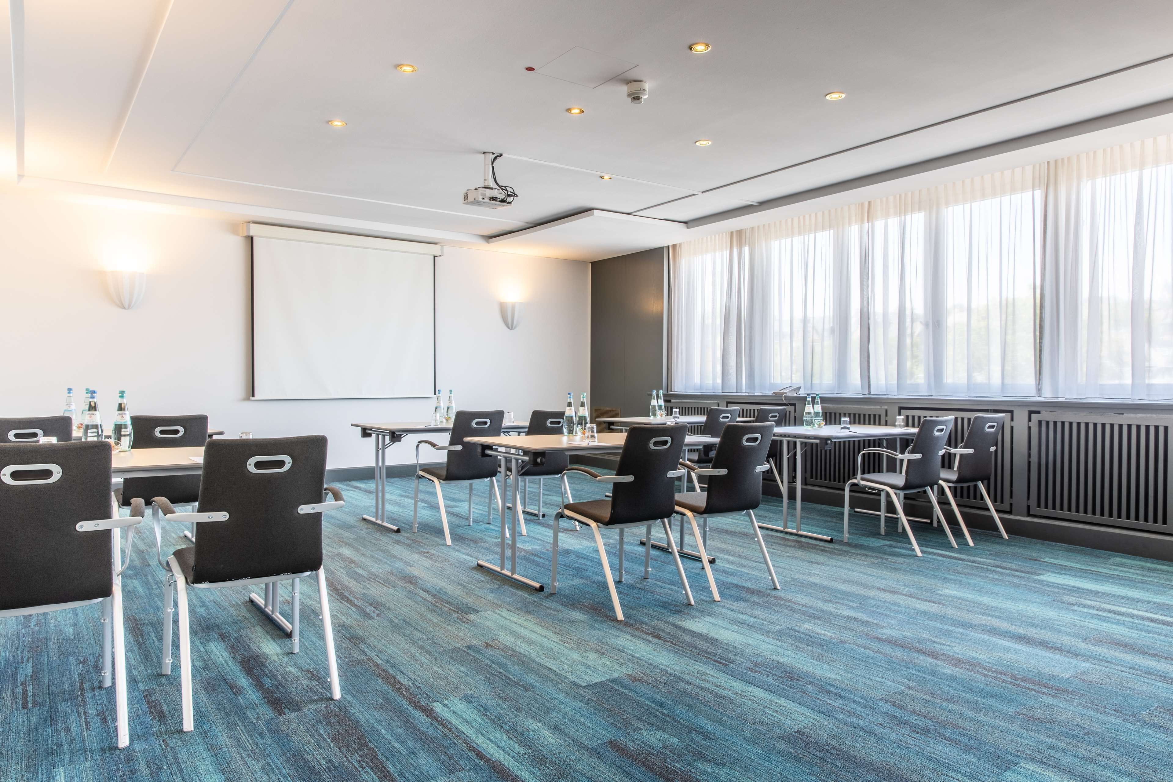 A conference room with a projector, whiteboard, and large windows with curtains.