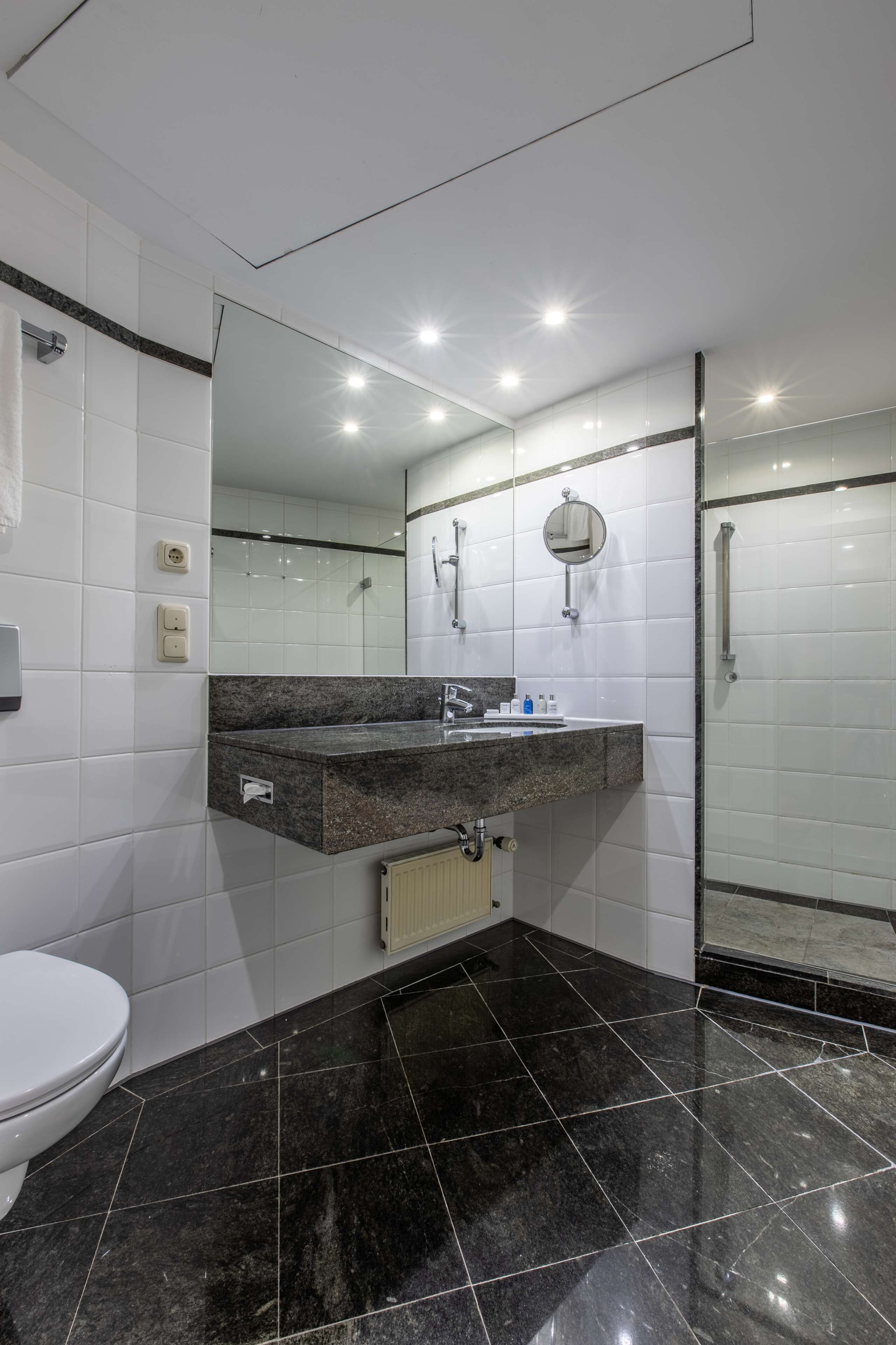 A modern bathroom with a black marble floor, a white toilet, a sink with a mirror, and a glass shower enclosure.