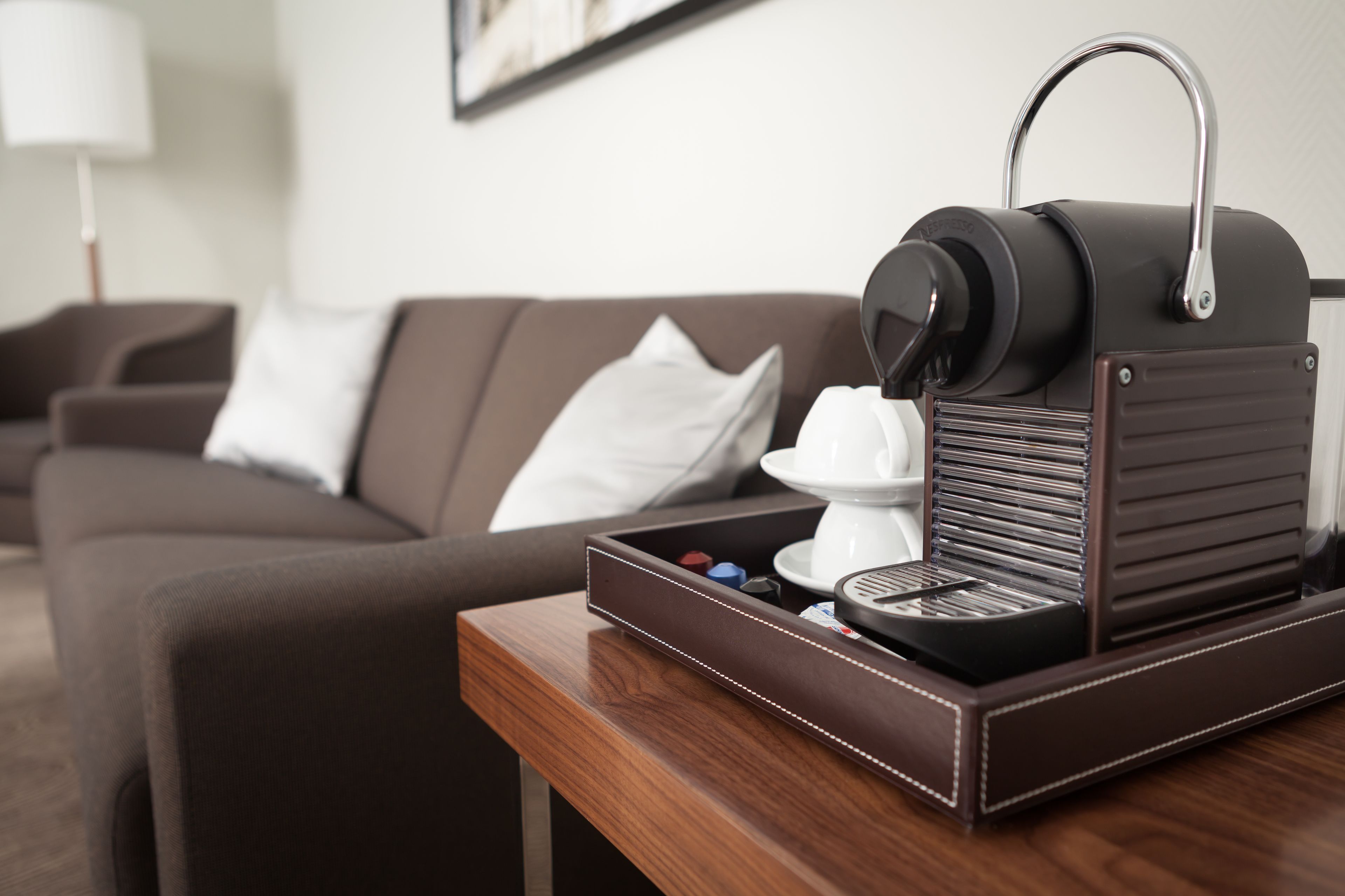 Eine Kaffeemaschine auf einem Holztisch, im Hintergrund ein braunes Sofa und ein weißes Kissen.