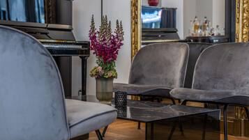 A modern living room with a piano, two grey upholstered chairs, a black coffee table, and a vase with purple flowers.