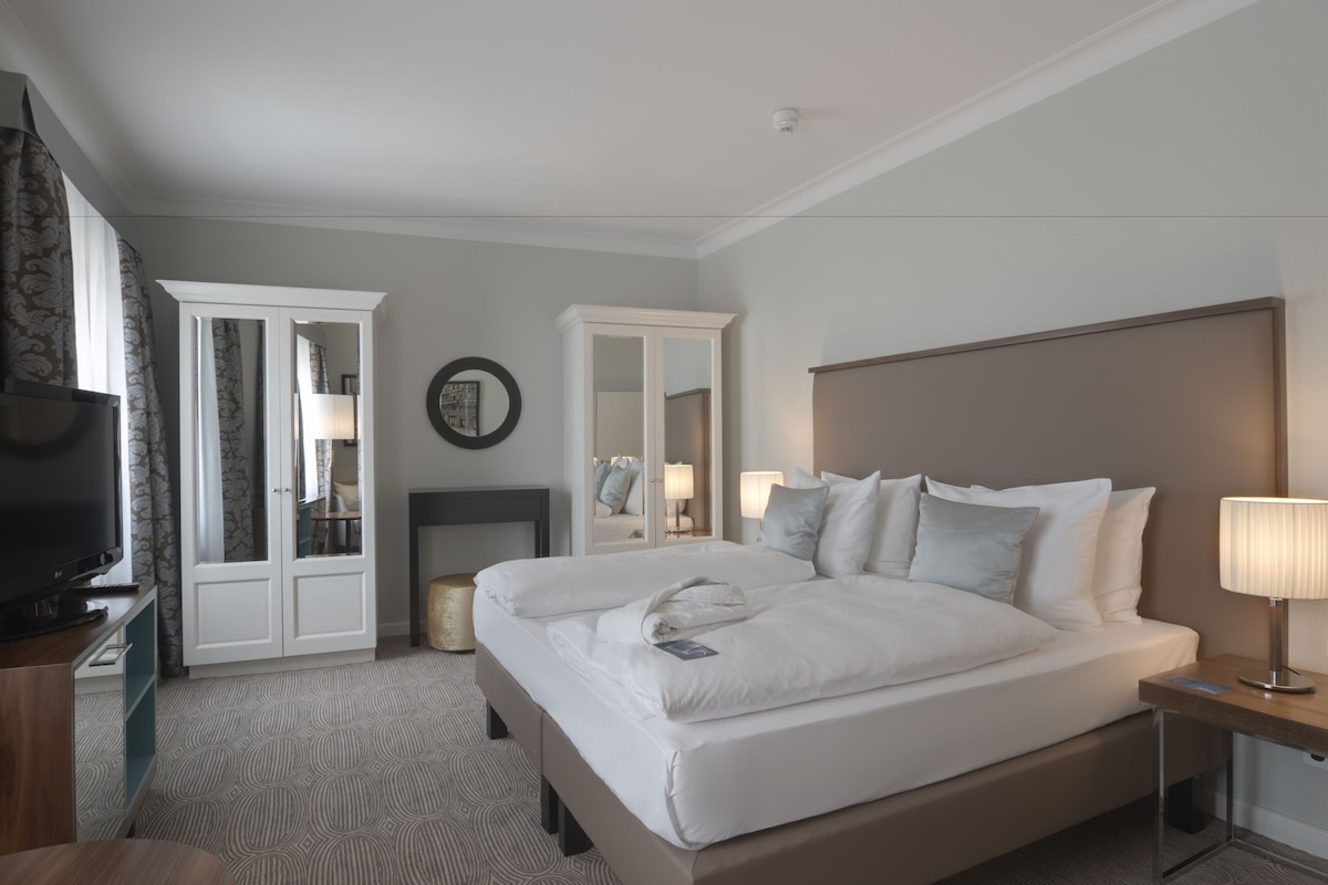 Una habitación de hotel con cama, televisor, armario, espejo y lámpara.