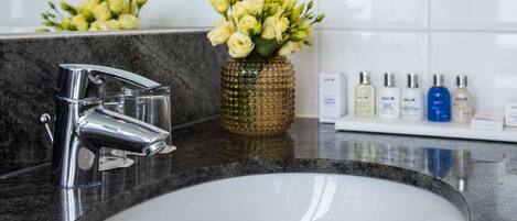 Un baño con un lavabo blanco, grifo cromado y un espejo encima. Hay flores en un jarrón sobre la encimera.