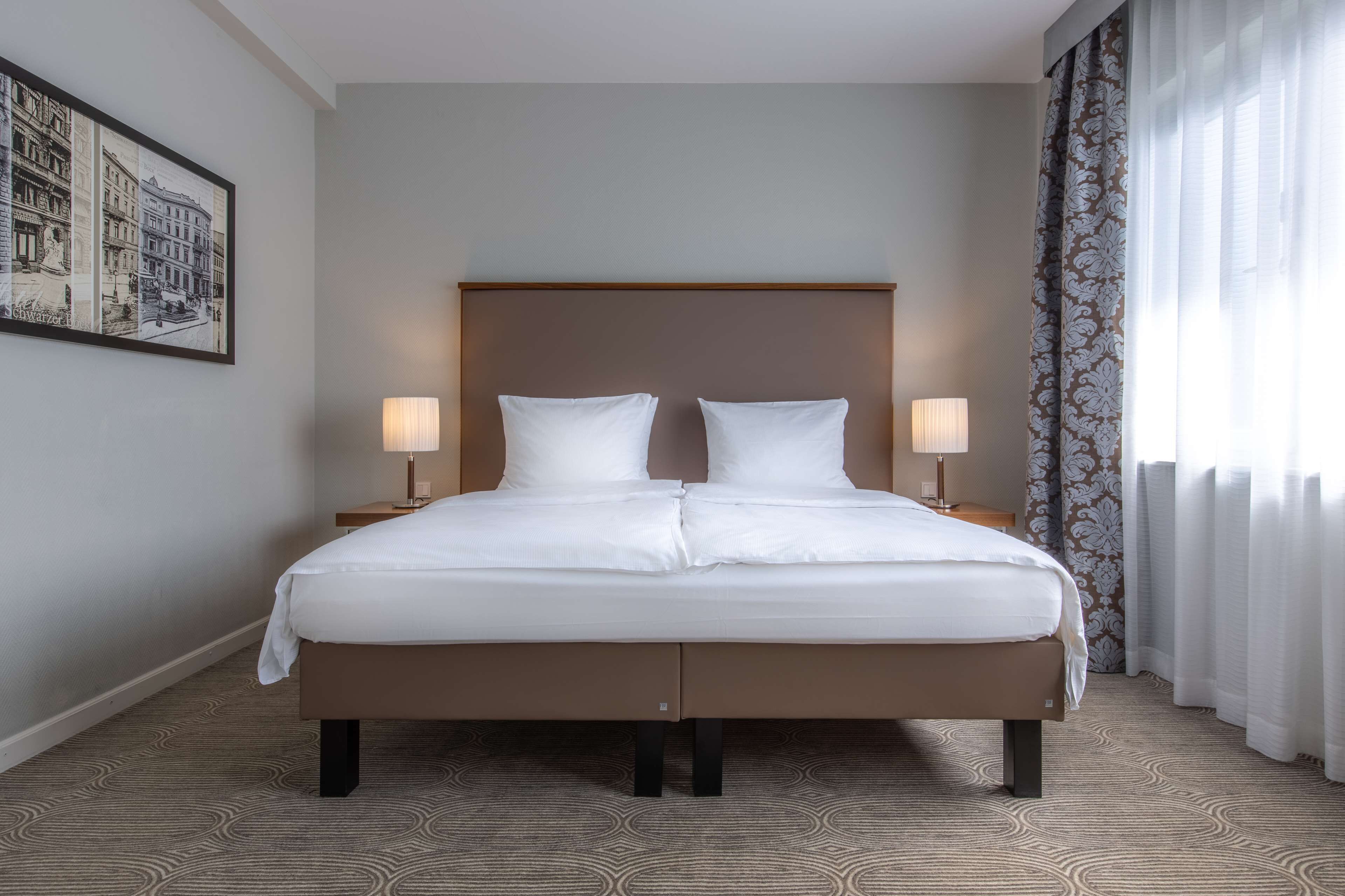 A hotel room with a large bed, two bedside lamps, a headboard, and a patterned carpet.