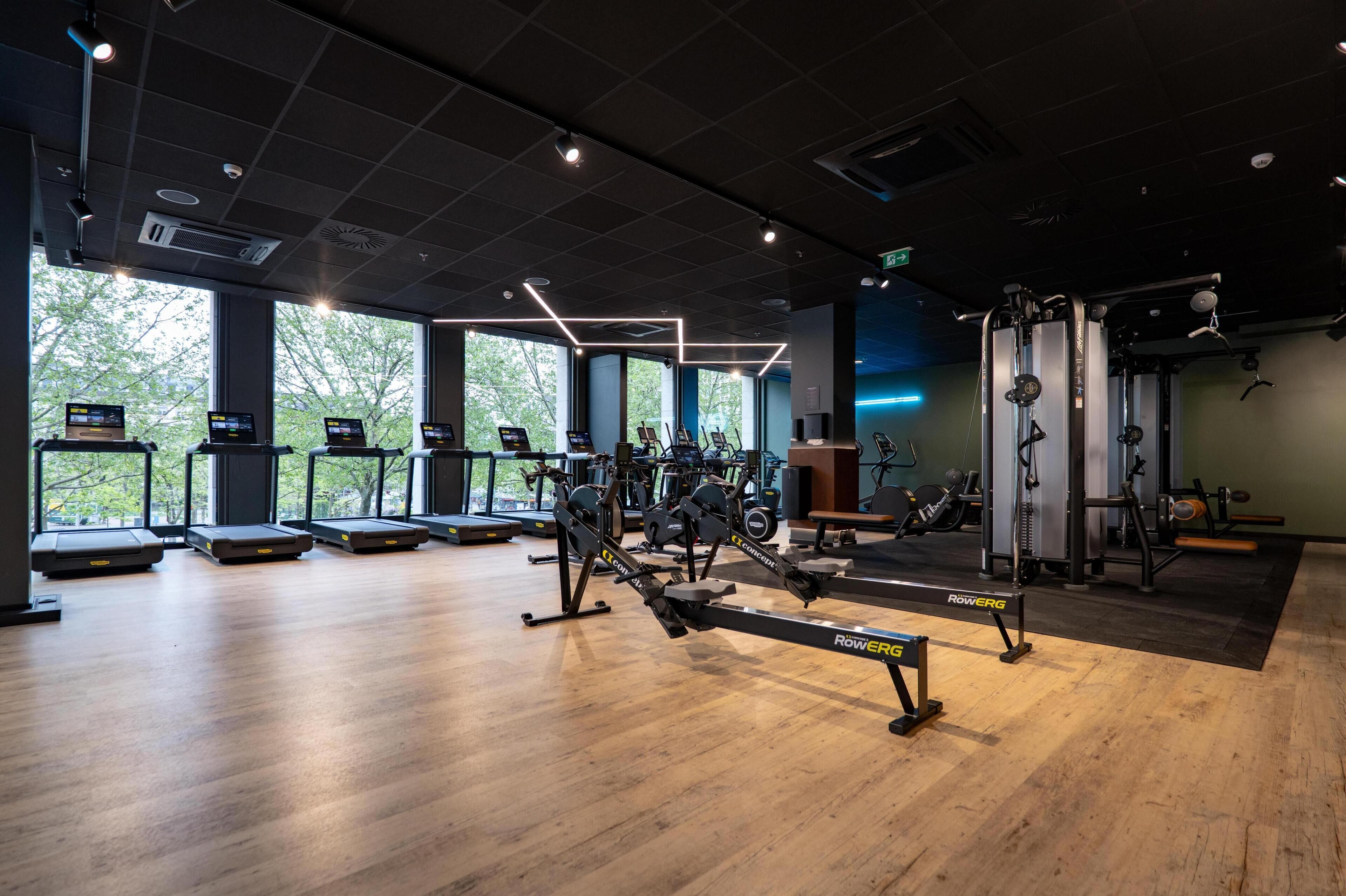 A gym with cardio machines, weightlifting equipment, and large windows.