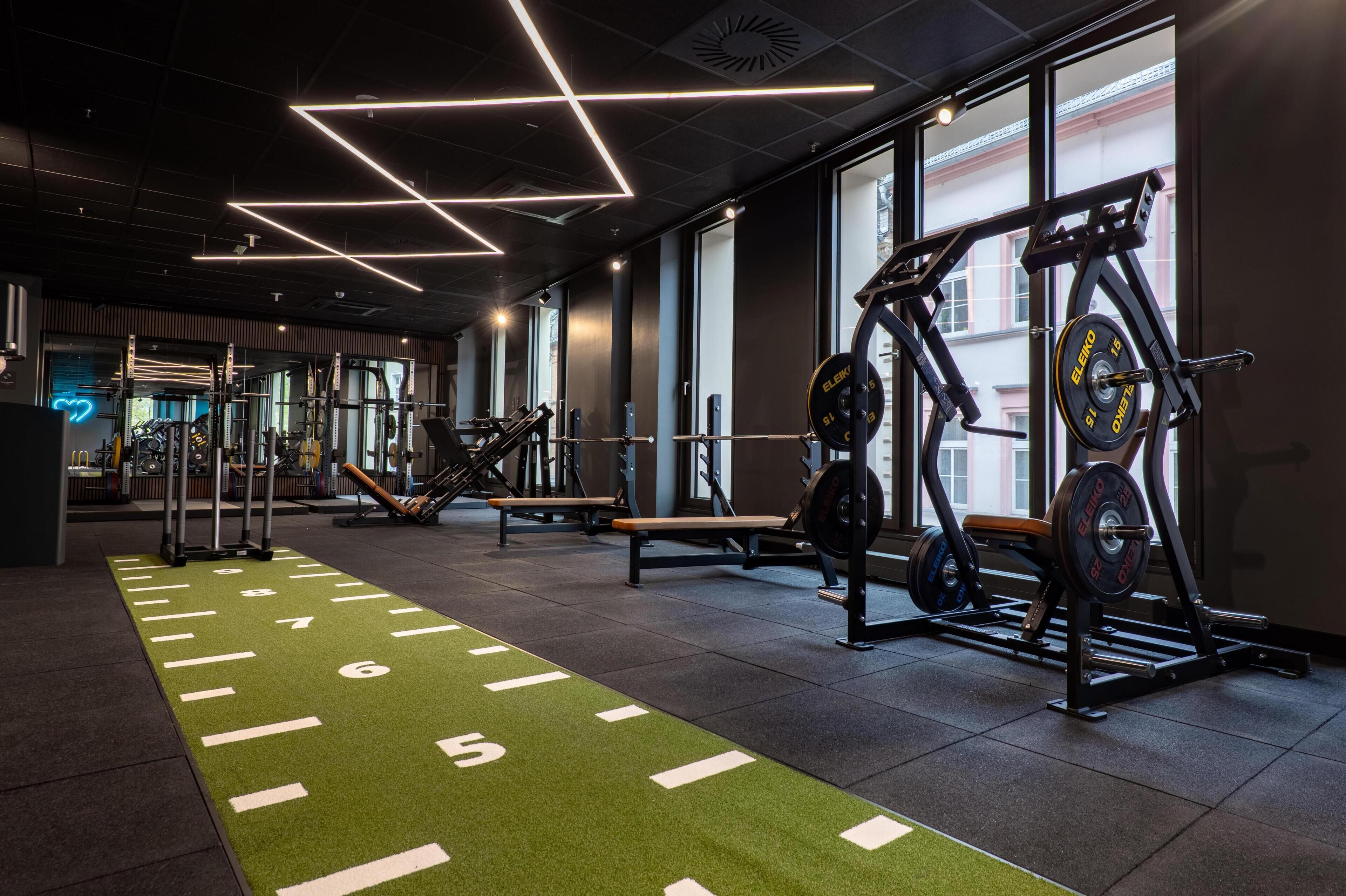 A gym with weightlifting equipment, a green running track, and large windows.