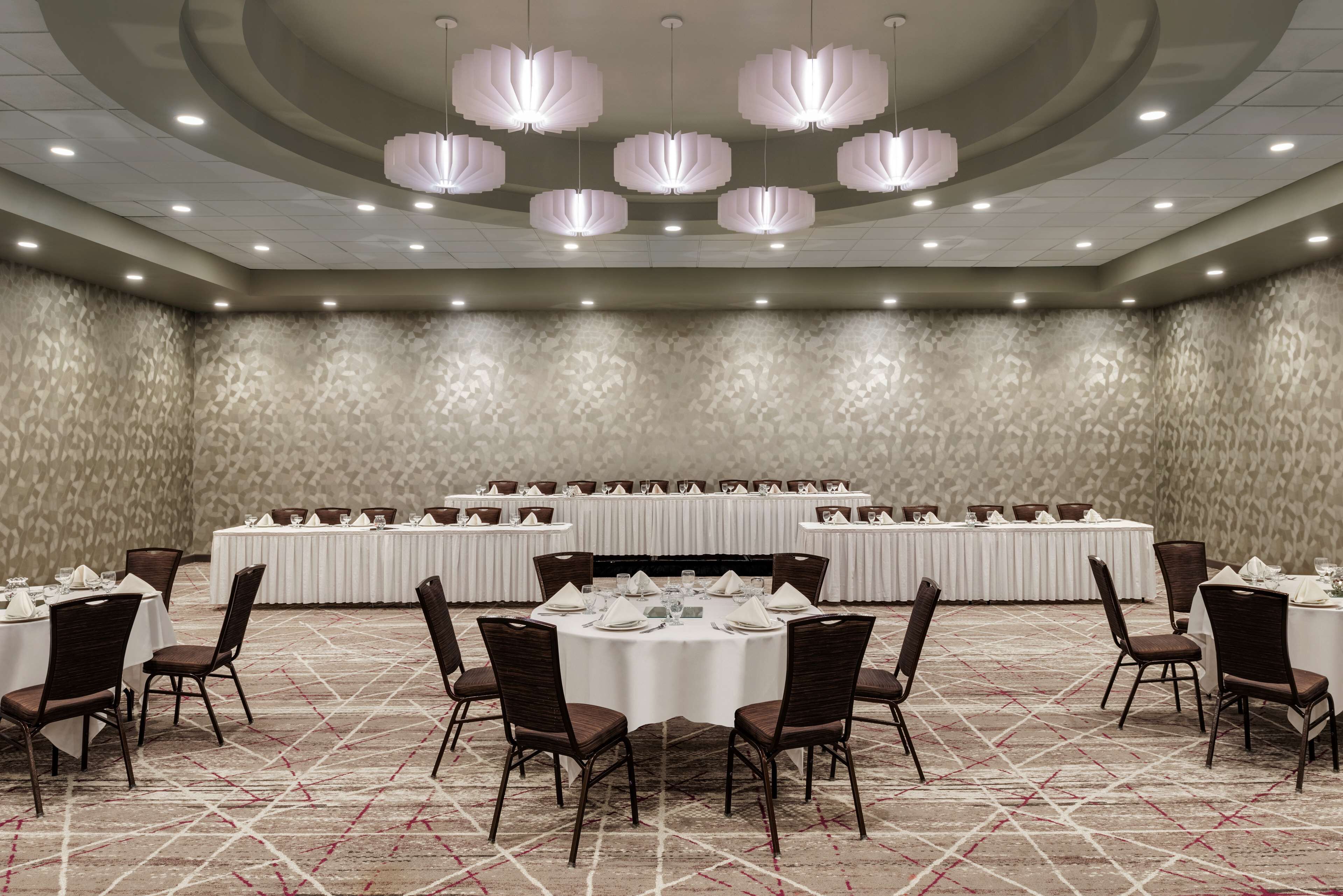 Une salle de banquet avec des tables rondes dressées pour le repas, équipées de chaises et de couverts.