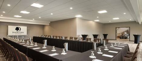 A conference room with long tables, chairs, and a projector screen displaying "DoubleTree by Hilton".