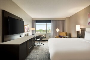 Habitación de hotel con una cama grande, un escritorio con silla, un televisor de pantalla plana y una ventana con cortinas.
