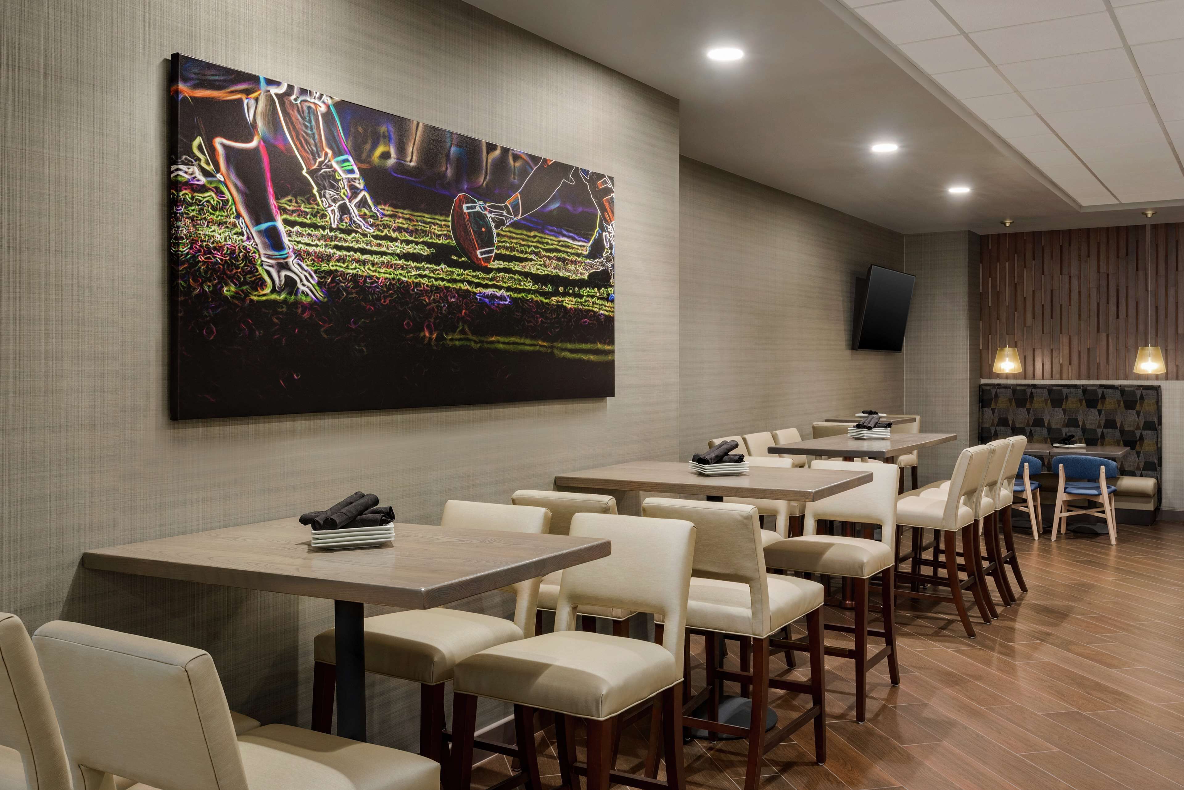Un restaurante con varias mesas y sillas, un cuadro abstracto grande en la pared, y un televisor de pantalla plana montado en la pared.