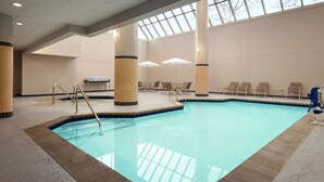 An indoor swimming pool with clear blue water, surrounded by beige and brown columns, and equipped with lounge chairs and umbrellas. - DoubleTree by Hilton St. Paul East (St. Paul)