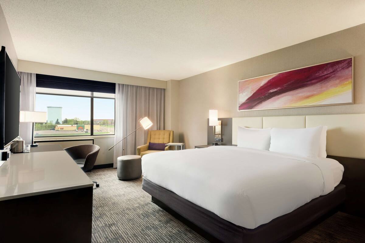 A hotel room with a large bed, a desk, a chair, a lamp, and a painting on the wall.