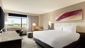Quarto de hotel com uma cama grande, uma escrivaninha, uma cadeira, um abajur e um quadro na parede.