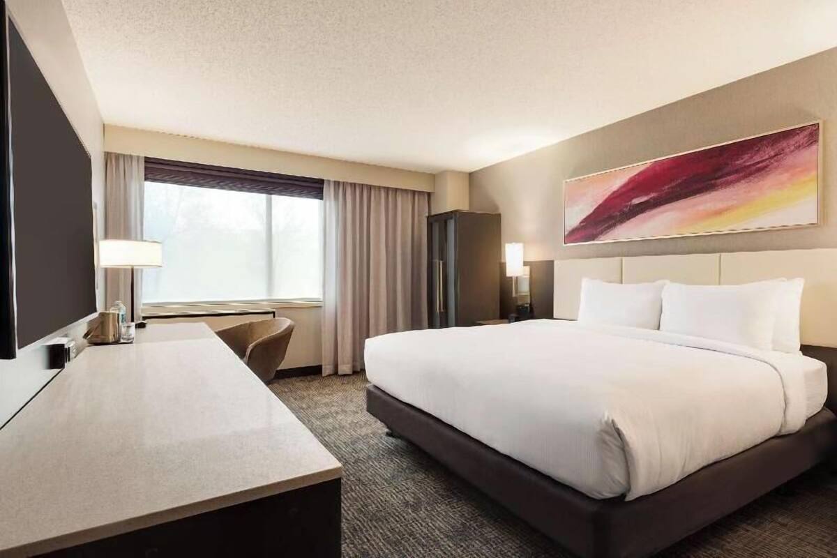 A hotel room with a bed, desk, chair, and a large abstract painting on the wall.