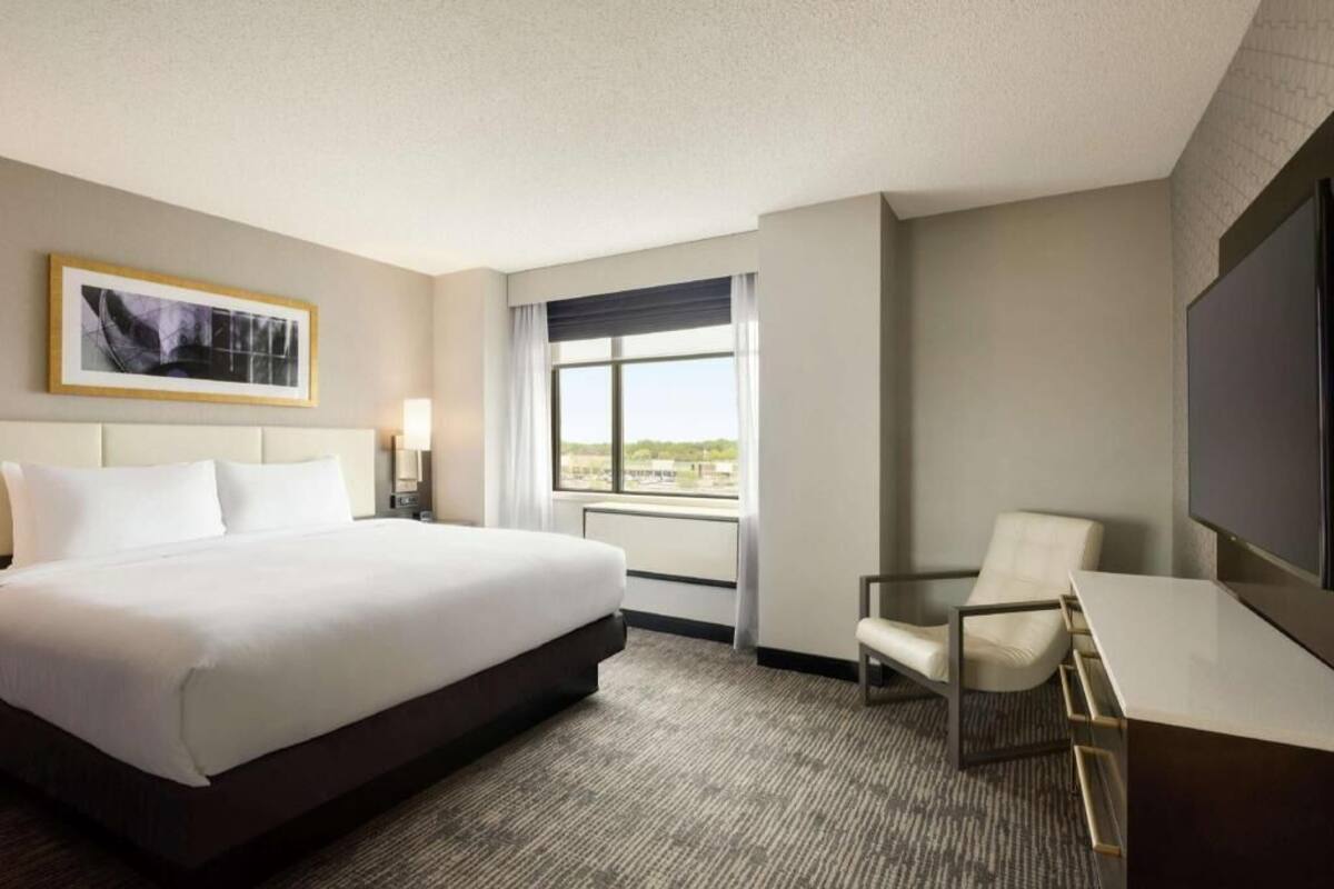 A hotel room with a large bed, a desk, a chair, a TV, and a window with a view.