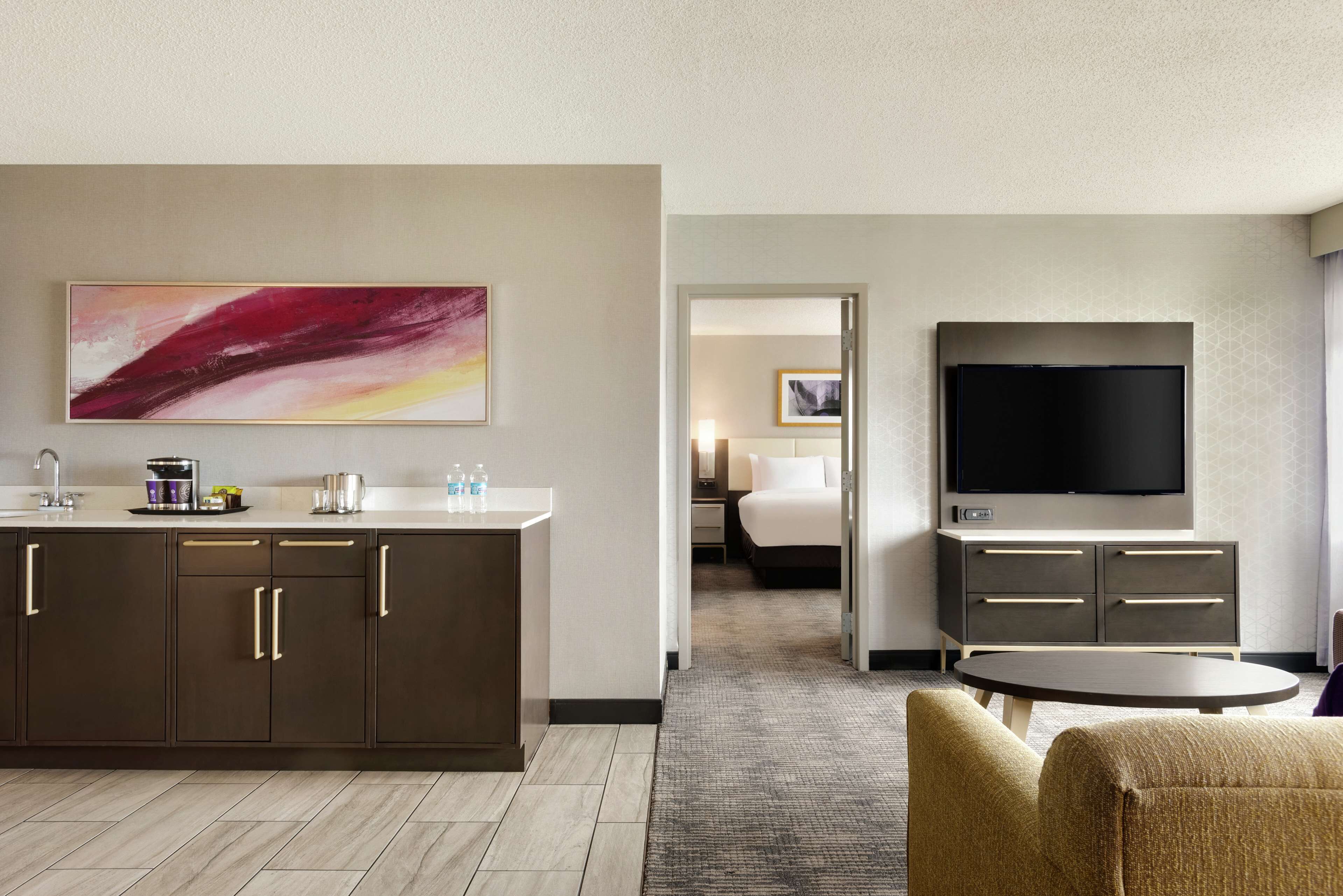 A hotel room with a kitchenette, a flat-screen TV, a bed, and a seating area with a small table.