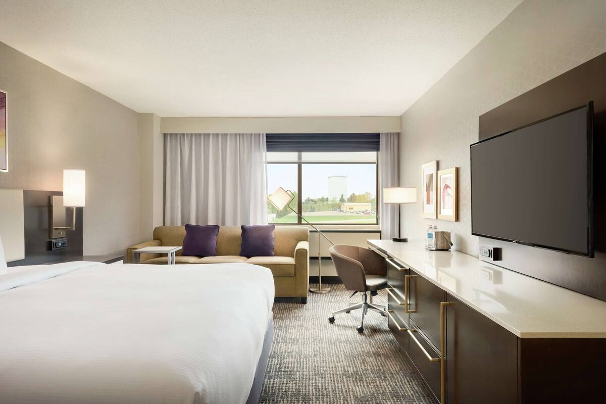 A hotel room with a large bed, a desk with a chair, a TV, and a window with curtains.