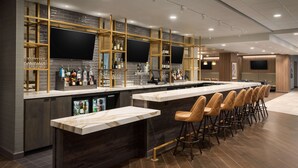 A modern bar area with a long counter, multiple stools, and a television screen. - DoubleTree by Hilton St. Paul East (St. Paul)