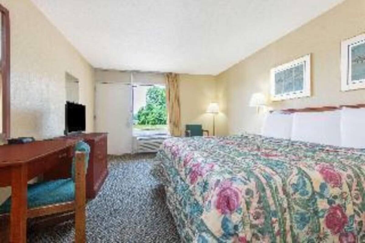 A hotel room with a bed, a desk, a chair, a lamp, and a window with curtains.