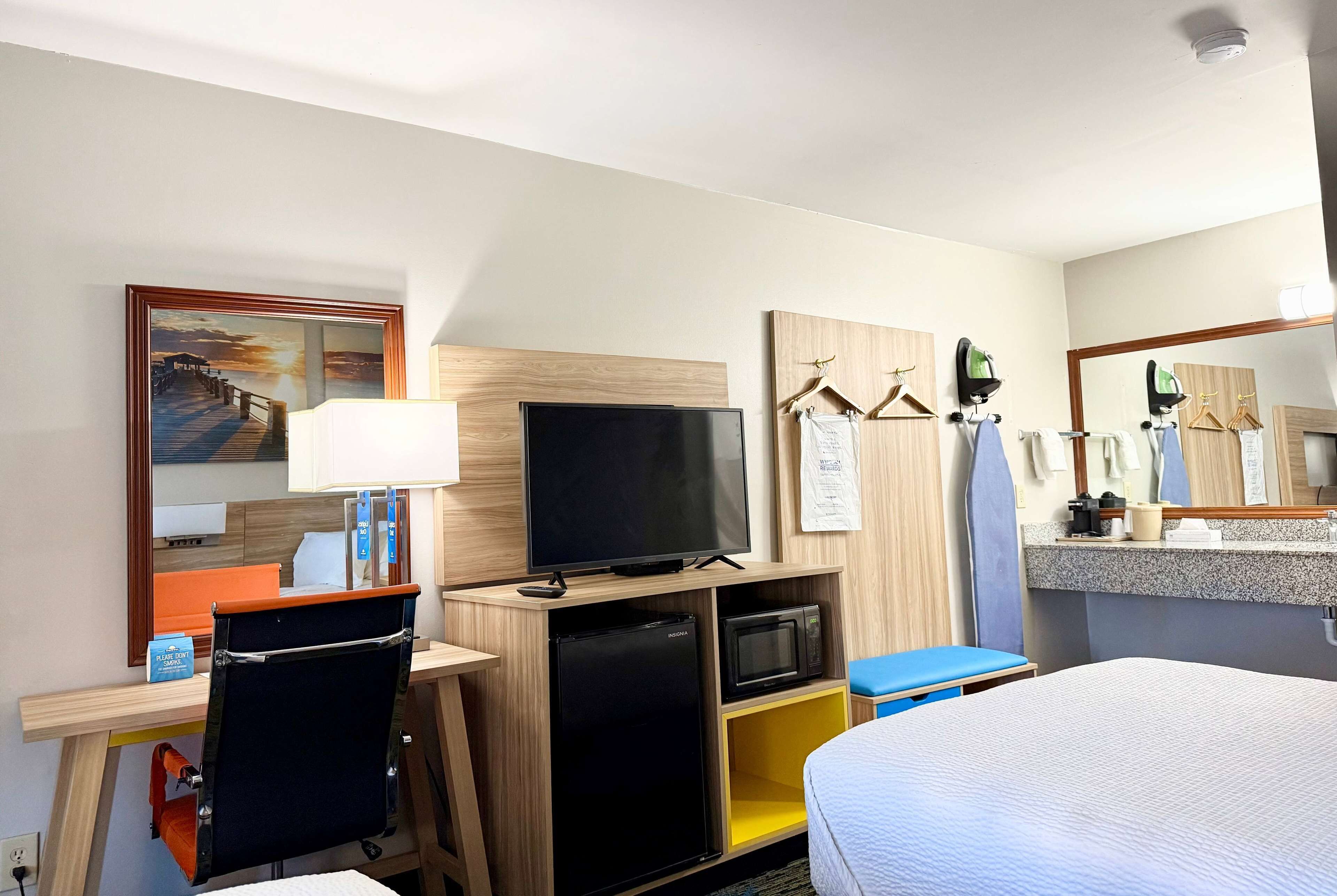 Habitación de hotel con cama, escritorio con computadora, televisión, microondas y refrigerador pequeño.