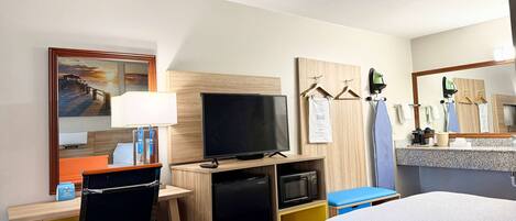 Habitación de hotel con cama, escritorio con computadora, televisión, microondas y refrigerador pequeño.