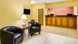 A reception area with a wooden reception desk, two leather armchairs, a lamp, and a flat-screen TV mounted on the wall. - Baymont by Wyndham Helena (Helena)