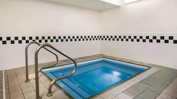 A swimming pool with a metal ladder, surrounded by tiled walls and floor.