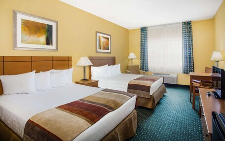 A hotel room with two beds, a desk, a chair, a TV, and artwork on the walls.