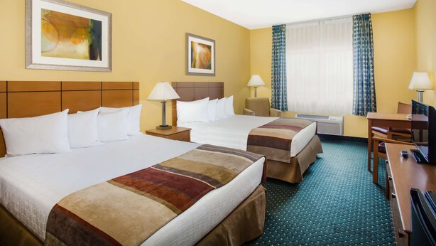 A hotel room with two beds, a desk, a chair, a TV, and artwork on the walls. - Baymont by Wyndham Helena (Helena)