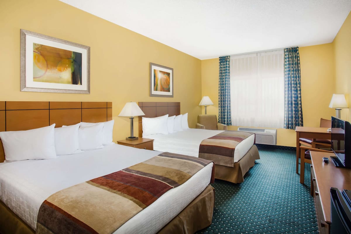 Ein Hotelzimmer mit zwei Betten, einem Schreibtisch, einem Stuhl, einem Fernseher und Bildern an den Wänden.