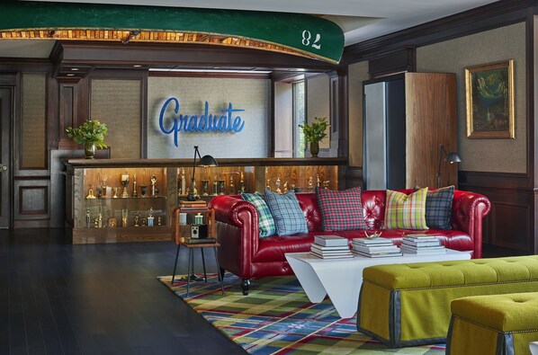 A lobby with a red leather sofa, a 'Graduate' sign, trophies, and a colorful rug.