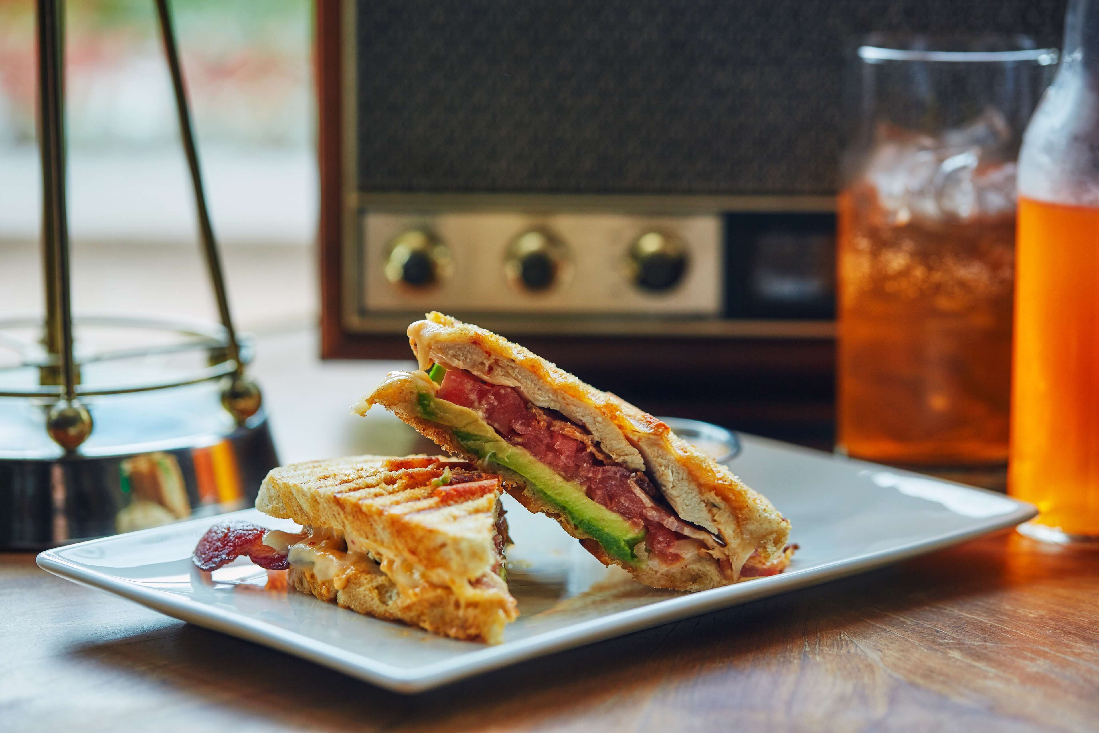 Un sándwich en un plato, un vaso de líquido ámbar y una radio antigua.