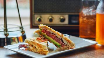 Un sándwich en un plato, un vaso de líquido ámbar y una radio antigua.