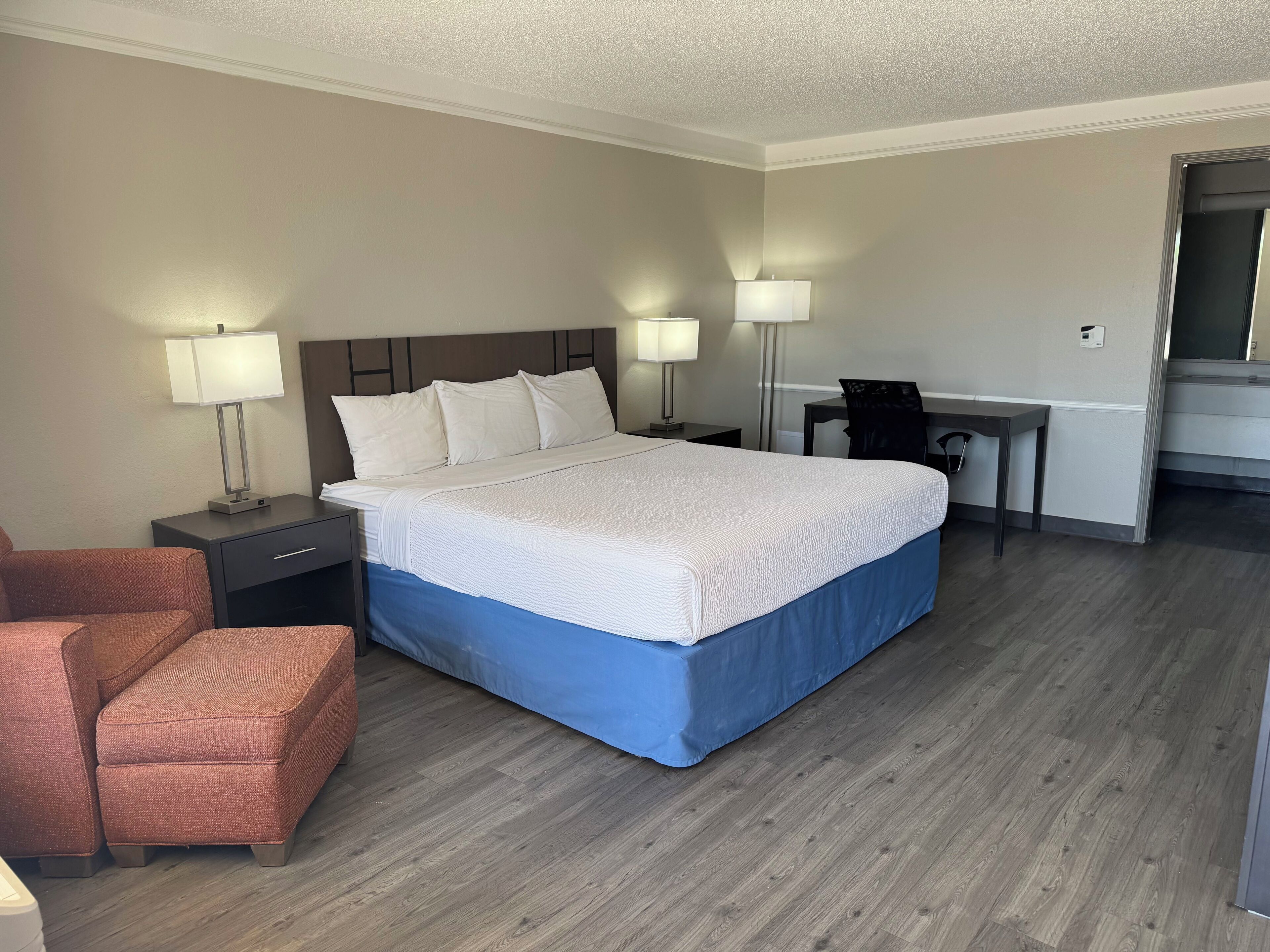 A hotel room with a large bed, two bedside tables with lamps, a desk, and a chair.