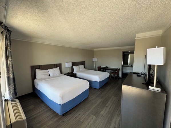 A hotel room with two beds, a desk, a chair, a lamp, and a TV.