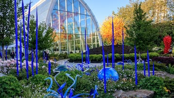 A modern glass building surrounded by a garden with blue and yellow glass sculptures.