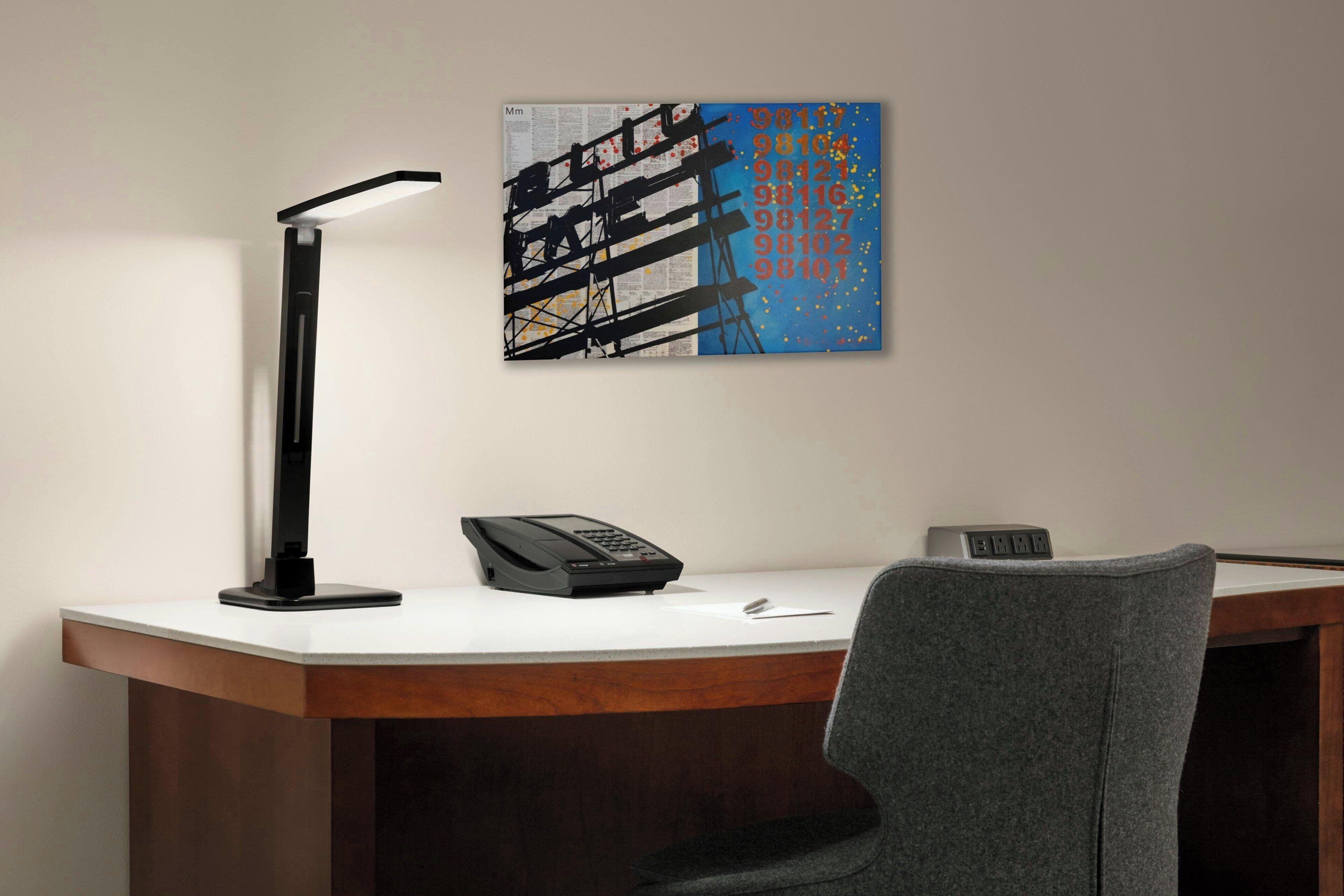 A desk with a modern lamp, a telephone, and a digital clock.