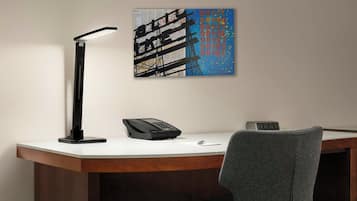 A desk with a modern lamp, a telephone, and a digital clock.