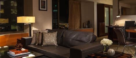A modern hotel room with a leather sofa, a desk with a lamp, and a view of the city at night.