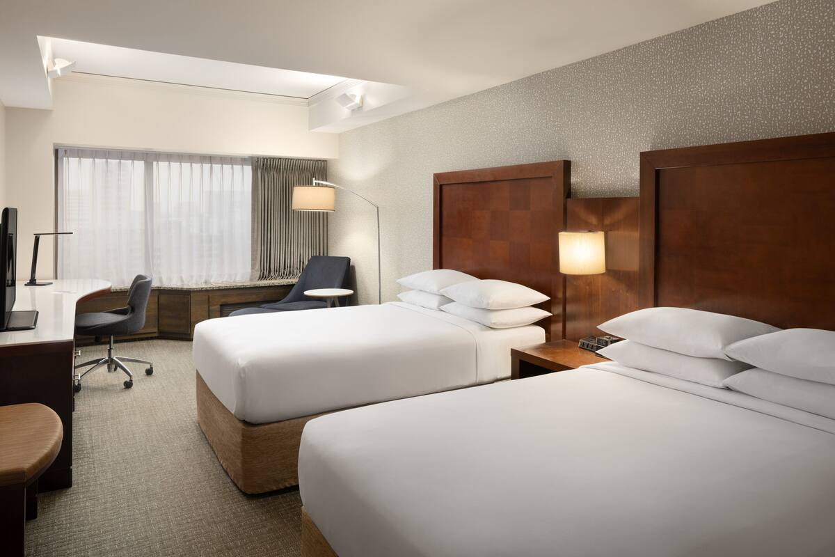 Ein Hotelzimmer mit zwei Betten, einem Schreibtisch, einem Stuhl und einem Fernseher.