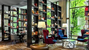 A modern library with bookshelves, comfortable seating, and large windows offering a view of greenery.
