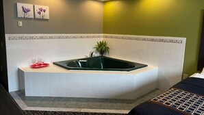 Un baño en esquina con una bañera independiente, una planta en maceta y dos cuadros con motivos florales en la pared.