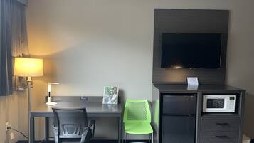 Habitación de hotel con escritorio, silla, lámpara, televisor, microondas y refrigerador pequeño.