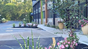 Un edificio moderno con estacionamiento, zonas ajardinadas con flores y un cielo despejado.